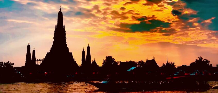  Silhouette of Wat Arun during a dramatic golden sunset over the Chao Phraya River in Bangkok, Thailand. Majestic temple structure framed by vibrant orange clouds and serene waters.