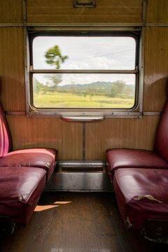 View from inside a vintage train carriage with red seats and a landscape view