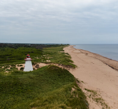 White lighthouse on a grassy coastal sand dune and empty beach.
