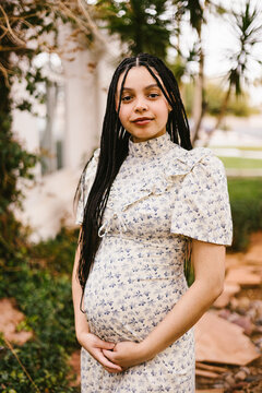 Pregnant woman with braids cradling her baby bump