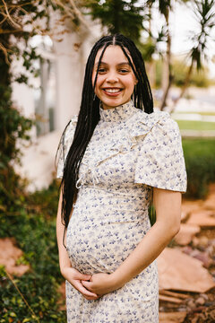 Happy pregnant woman with braids cradles her belly