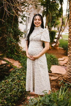 Happy pregnant woman cradling baby bump outdoors