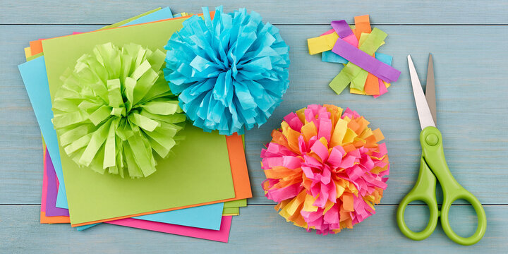 Crafting colorful tissue paper pom-poms with scissors and colored paper. Three vibrant pom-poms in shades of green, blue.