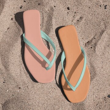 Pastel flip flop sandals on sandy beach background