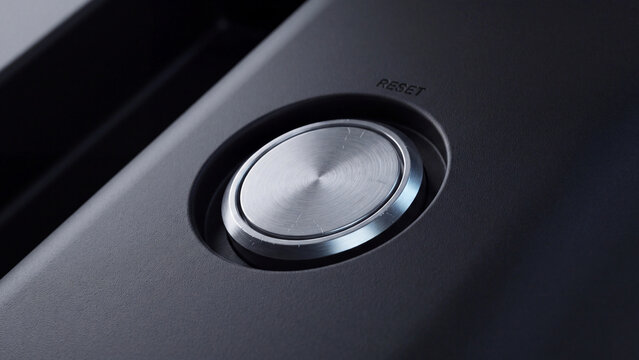 Metal button with a brushed texture and reset text is embedded in a sleek dark grey control panel.
