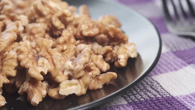 Close up camera movement over walnut kernels on black plate placed on purple checkered tablecloth