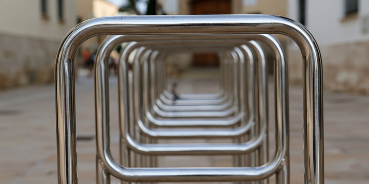 A close-up shot of a metal bicycle rack, creating a sense of repetition and perspective. The rack is made of sleek, silver metal bars, forming a geometric pattern that recedes into the background.