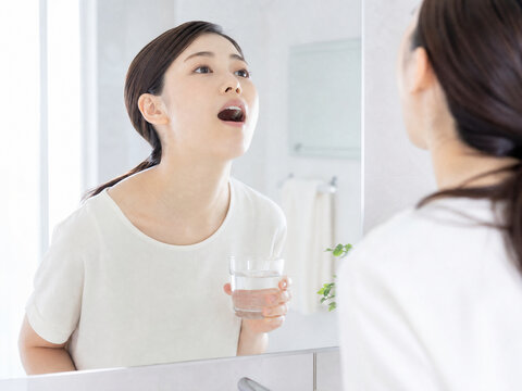 洗面所でコップの水を使い上を向いてうがいをする女性