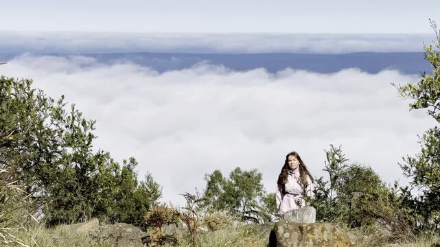 A girl walks and admires the view from the summit, with thick clouds emerging above the eucalyptus bush and a clearing, Mount Macedon, Macedon Ranges, near Melbourne, Victoria, Australia.