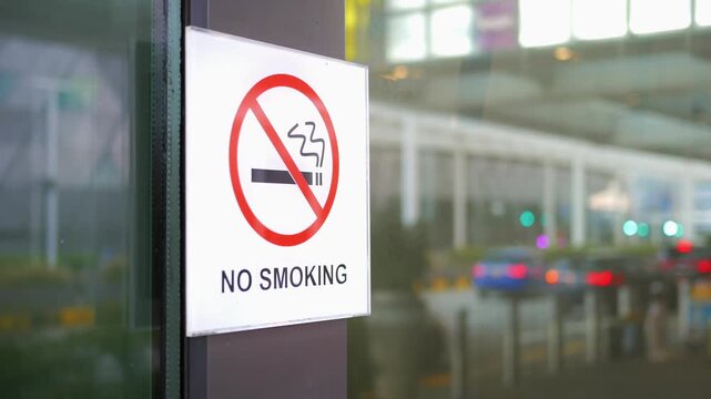 No smoking sign at airport terminal entrance with blurred traffic and cars in background