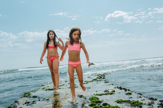 Two Sisters Walking on Mossy Coastal Rocks at Low Tide on a Sunny Day