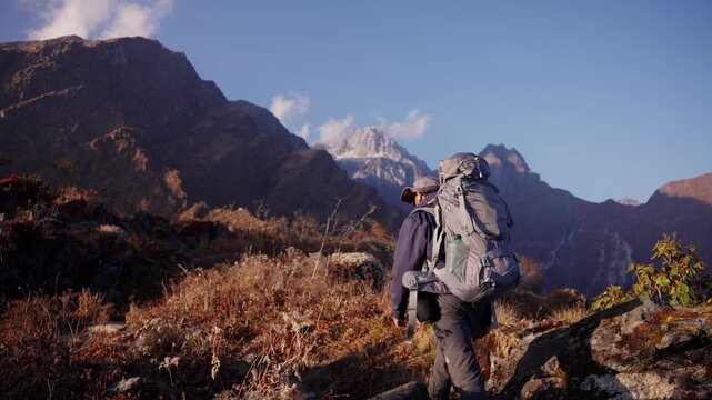 Triumphant trekker stands on a rocky outcrop with arms raised in celebration as the snow capped Saipal Himal peak rises majestically behind