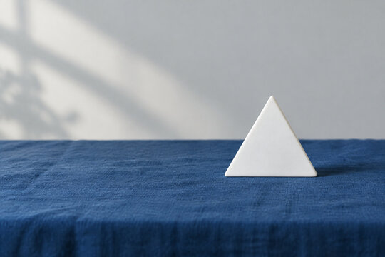 Single white equilateral triangle object on deep blue linen, calm still life for editorial concept