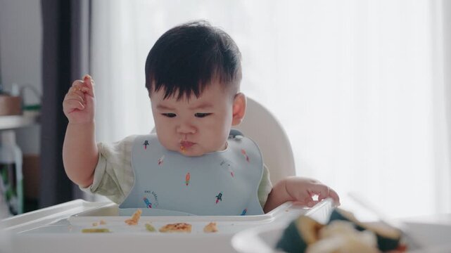 Asian toddler eating breakfast in high chair, baby-led weaning BLW concept