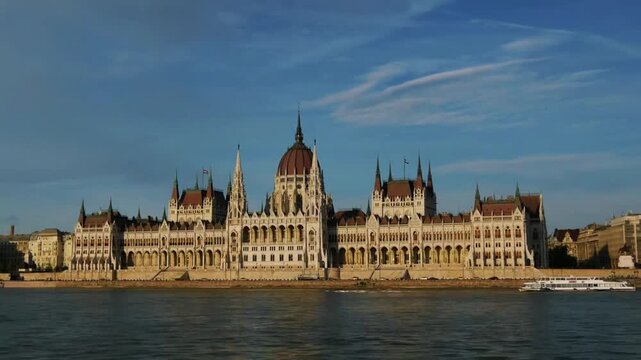 Historic hungarian parliament building along danube river with cruise boat passing by during golden hour