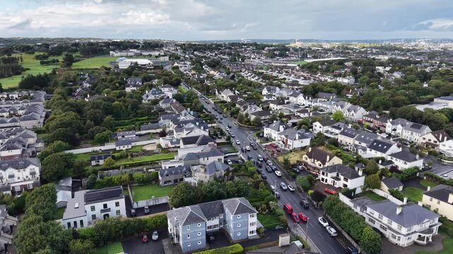 Aerial drone footage overlooking the residential neighborhoods of Salthill and Galway, Ireland. The elevated view shows traditional and modern homes, landscaped gardens, tree-lined streets, busy roads