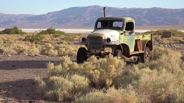 Old military truck rusting in a desert landscape during day with mountains in background, abandoned vehicle in death valley california.