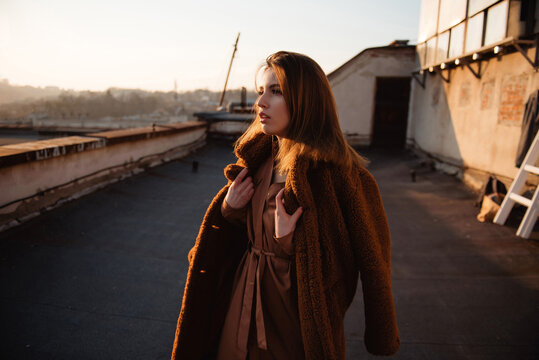 Woman in warm coat on rooftop during golden hour sunset