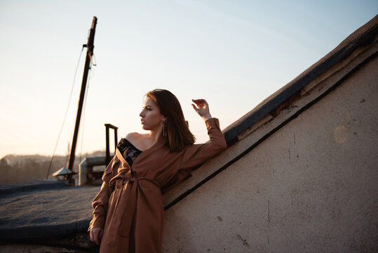 Woman in stylish trench coat posing on rooftop at golden hour sunset