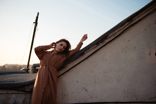 Woman in trench coat enjoying golden hour sunset on urban rooftop