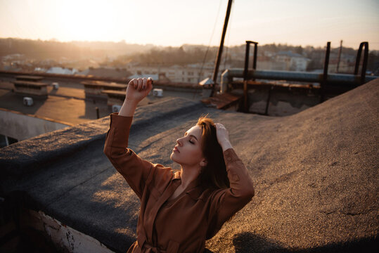 Woman enjoying golden hour sunset on a city rooftop with arms raised