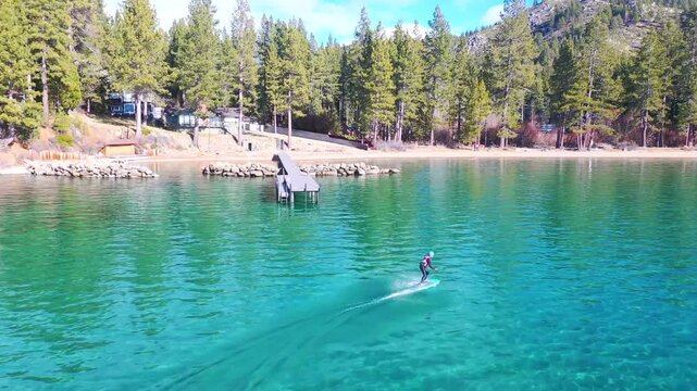 Woman on electric hydrofoil surfboard gliding across clear lake tahoe water, showcasing stunning scenery and outdoor recreation.