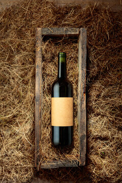 Bottle of red wine in an antique wooden box on a table covered with hay.