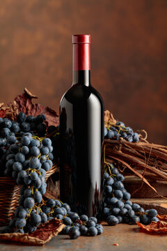 Bottle of red wine with blue grapes on a brown background.