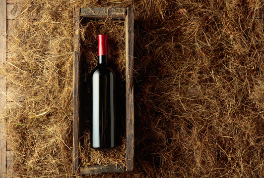 Bottle of red wine in an antique wooden box on a table covered with hay.