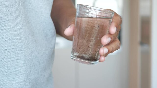 Man holding glass of murky water with sediment