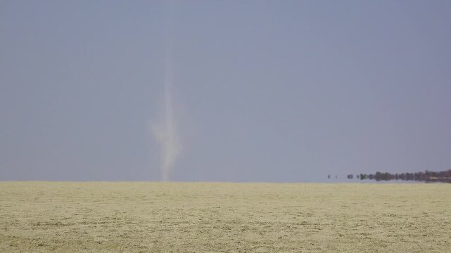 Small dust devil spinning across arid desert landscape during hot sunny afternoon.