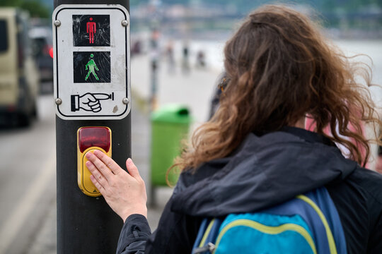 Woman pressing a pedestrian crossing request button at a traffic light signal on a city street in Budapest, Hungary