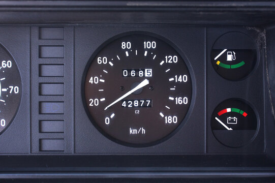Close-up dashboard old black car, featuring round analog speedometer with white needle and scale, an odometer, fuel gauge, and battery charge indicator.