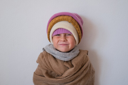 little girl wrapped in warm scarf wearing several knitted winter beanies