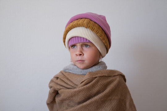 Thoughtful little girl wrapped in warm wool scarf wearing stacked winter beanies