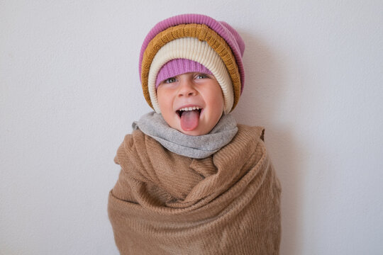  girl sticking tongue out wrapped in warm scarf wearing multiple winter beanies