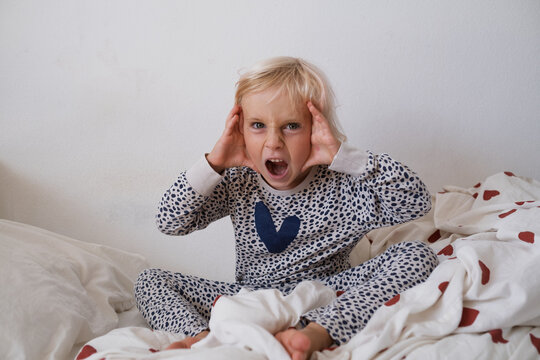 Angry little girl shouting and waving hands in bed throwing morning tantrum