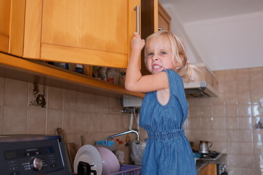  girl climbing kitchen counter making funny grimace while opening cabine