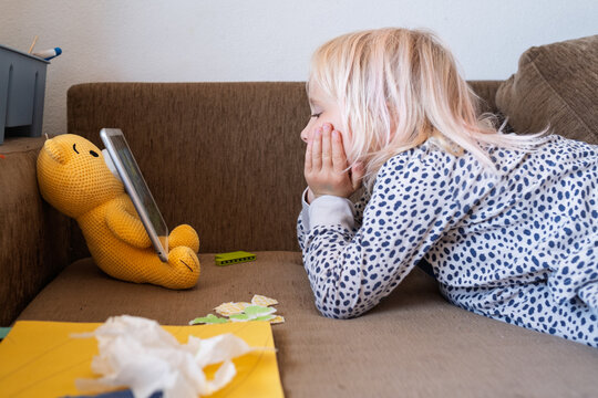  blonde girl lying on sofa watching cartoons on digital tablet