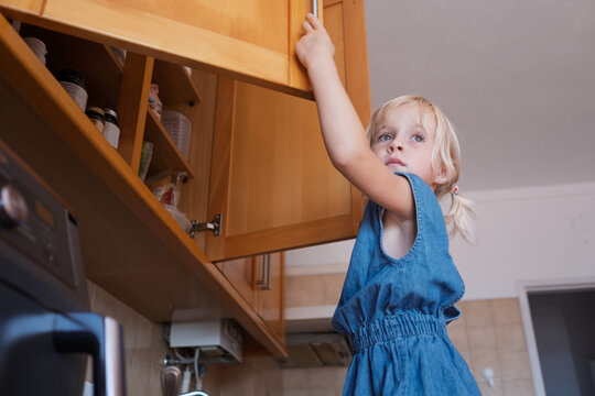  girl climbing kitchen counter making funny grimace while opening cabine