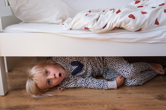 girl hiding under a white wooden bed 
