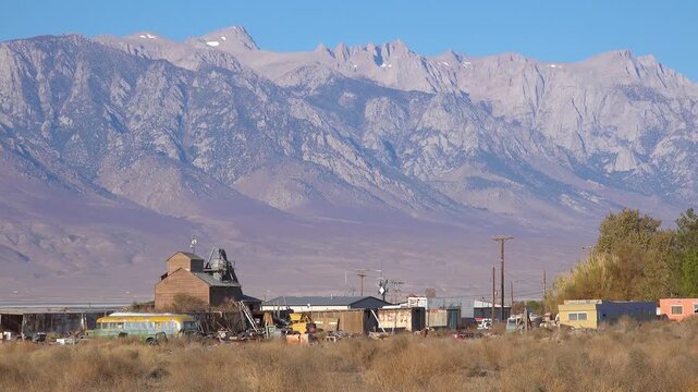 Scenic view of a rustic desert compound with tall mountain ranges in the background under clear blue sky during the day.