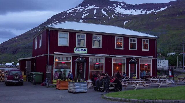 Aldan cafe building nestled in mountainous landscape with people relaxing outdoors on a calm evening.