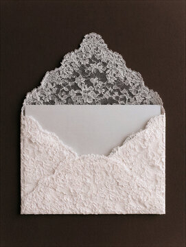 White lace envelope with delicate floral texture and open flap, isolated on dark background, creating elegant romantic stationery composition for wedding or invitation design
