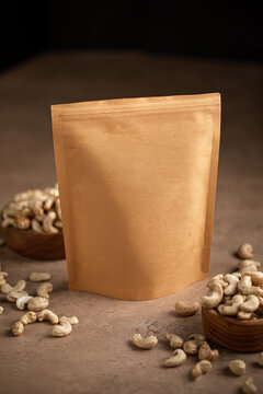 Blank craft paper zipper pouch packaging mockup surrounded by raw cashew nuts on stone table vertical