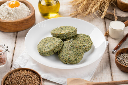 Raw turkey meat patties with spinach and vegetables on white plate surrounded by rustic ingredients