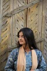 Fototapeta premium Candid portrait of a calm South Asian woman standing by a rustic wooden door