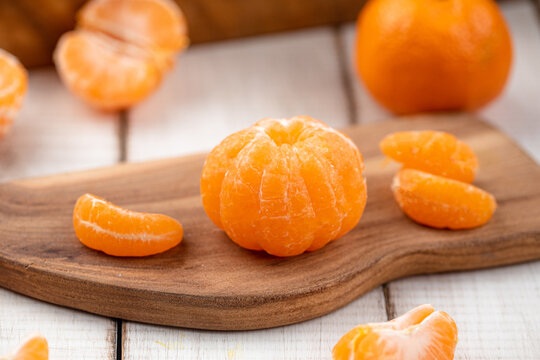 Fresh peeled mandarin tangerine fruit and slices on wooden cutting board on white rustic table