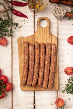 Uncooked fresh homemade sausages for grill on wooden cutting board with herbs and cherry tomatoes on white wood table