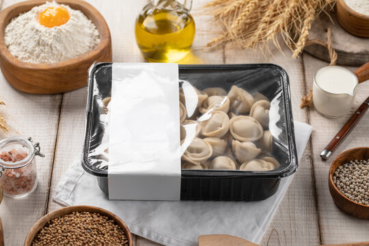 Raw frozen meat pelmeni dumplings packed in plastic tray container with blank label mockup on rustic table